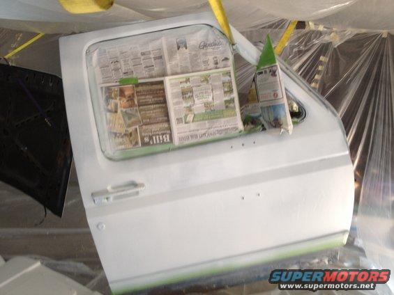 White vehicle door covered in newspaper and plastic sheeting, undergoing paintwork