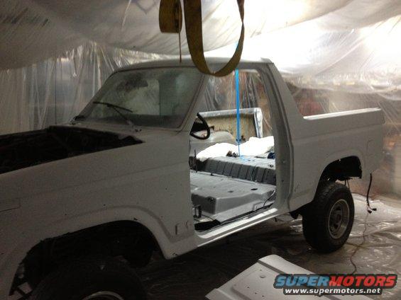 White Ford Bronco in a paint booth, doors open, interior stripped, hood up