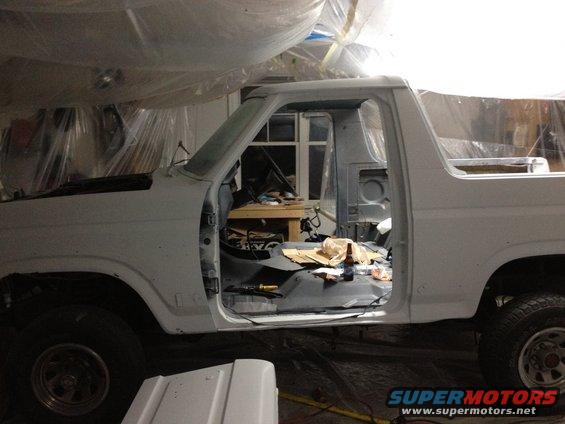 Side view of a white 1986 Ford Bronco undergoing repairs, doors removed