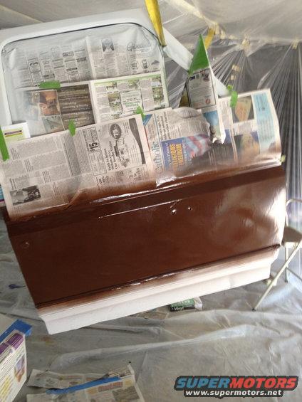 Car door covered in newspaper for painting, with brown paint applied