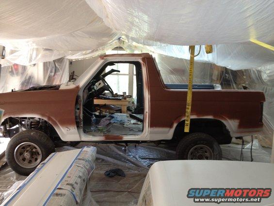 Brown and white Ford Bronco in side view, undergoing restoration with doors open and hood up