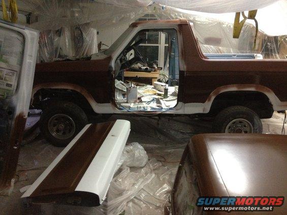 Brown and white Ford Bronco in garage with doors removed, undergoing paintwork