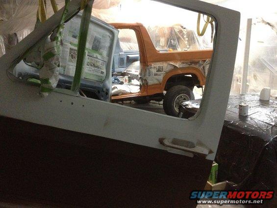 View through an open door of a Bronco being worked on, with another vehicle partly visible behind it