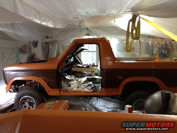 Orange and brown Ford Bronco in a garage, doors open, under plastic sheeting
