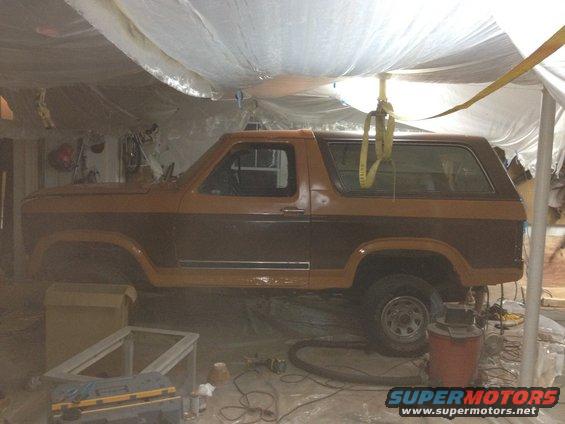 Two-tone brown Ford Bronco parked inside, covered with plastic sheeting