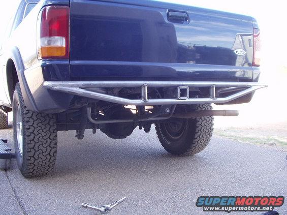 Rear view of a blue Ford Ranger pickup truck with a custom metal bumper and trailer hitch receiver. A wrench lies on the ground