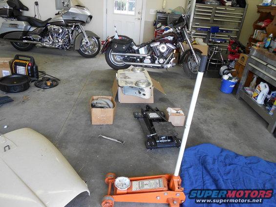 Two motorcycles parked in a garage with tools and car parts on the floor