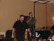 1992 Ford Taurus - A man speaks into a microphone while another man walks past him on a stage during an event.