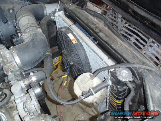 Engine bay with radiator, fan, and hoses. Yellow hazard sticker on fan shroud