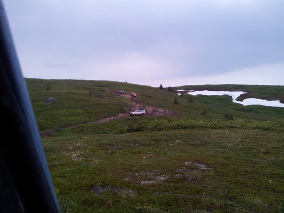Silver SUV on a dirt path on a grassy hill with snow patches