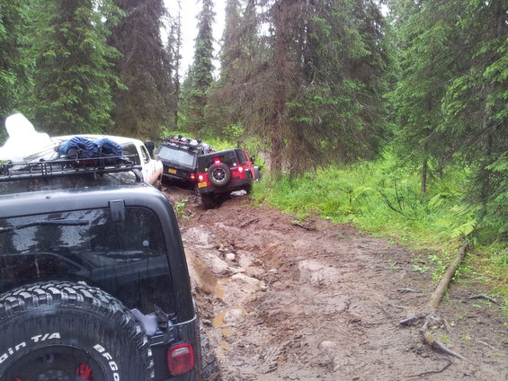 Several off-road vehicles stuck in a muddy forest trail