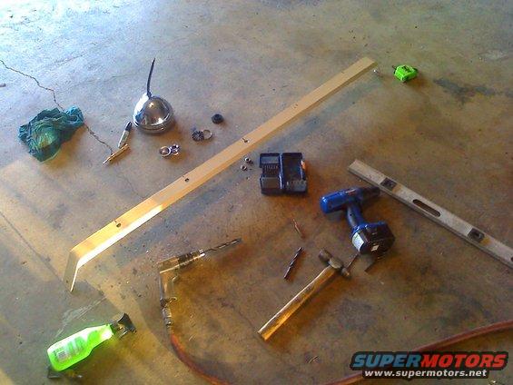Tools including drills, hammer, level, and oil can scattered on concrete floor with wood plank and spray bottle
