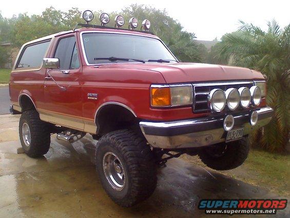 Red Ford Bronco with a lift kit, off-road lights on the roof and bumper, and large tires