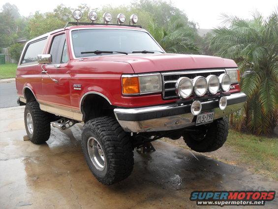 Red 1990 Ford Bronco with a lift kit and off-road lights on the front