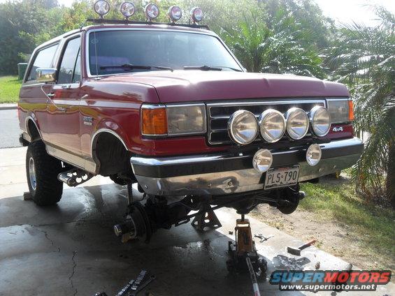 Red 1990 Ford Bronco with lift kit and roof lights, front view