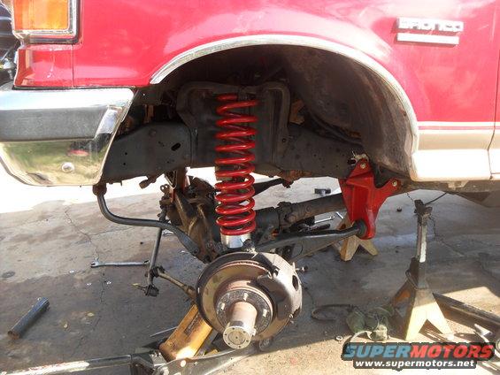 Red 1990 Ford Bronco front driver's side suspension with red coilover and lifted chassis on jack stands