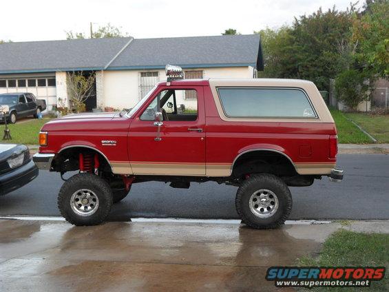 Red Ford Bronco, lifted with big tires, parked on a street