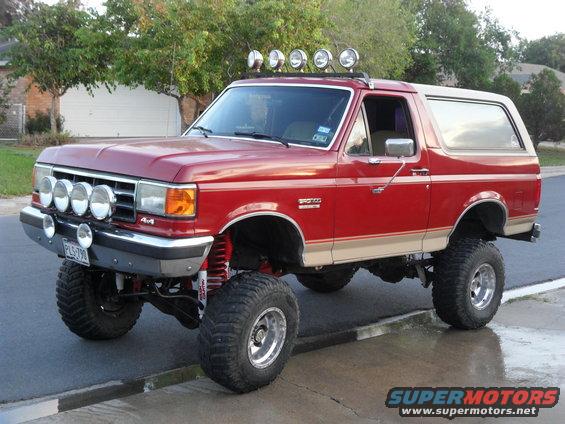 Red 1990 Ford Bronco with tan trim, lifted suspension, and roof-mounted lights