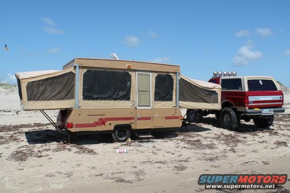 Red and white 1990 Ford Bronco towing a pop-up camper on a beach