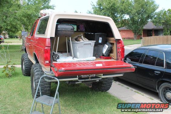 1990 Ford Bronco rear view, tailgate open, showing a grill and storage bins inside. Lifted suspension and large tires are visible