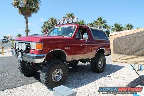 Red 1990 Ford Bronco with off-road lights and lifted suspension parked next to a camper
