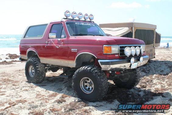 1990 Ford Bronco, red, lifted with off-road lights on beach