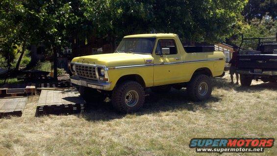 Yellow 1978 Ford Bronco with off-road tires parked in a grassy area next to a black Dodge pickup truck
