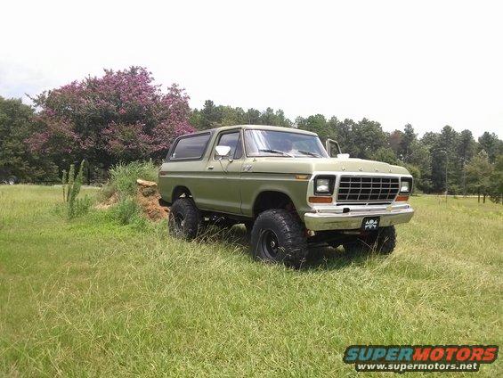 Green lifted Ford Bronco parked in a grassy field with trees in the background