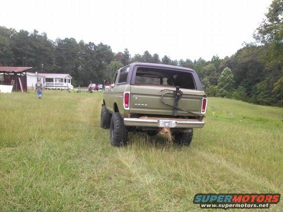 Olive green Ford Bronco with a spare tire mount on the rear, parked in a grassy field