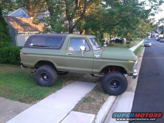 Olive green 1978 Ford Bronco with black top, lifted suspension, and large tires parked on a sidewalk