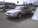 2003 Ford Crown Victoria - A silver 2003 Ford Crown Victoria is parked in a lot with other vehicles and commercial buildings in the background.