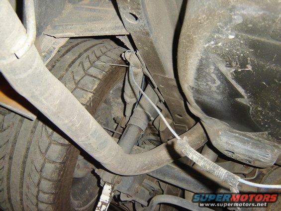 Underside view of a car's rear tire and suspension components. Shows exhaust pipe and wiring
