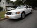 1999 Ford Crown Victoria - A white Ford Crown Victoria is parked on a residential street, with a white pickup truck in the background.