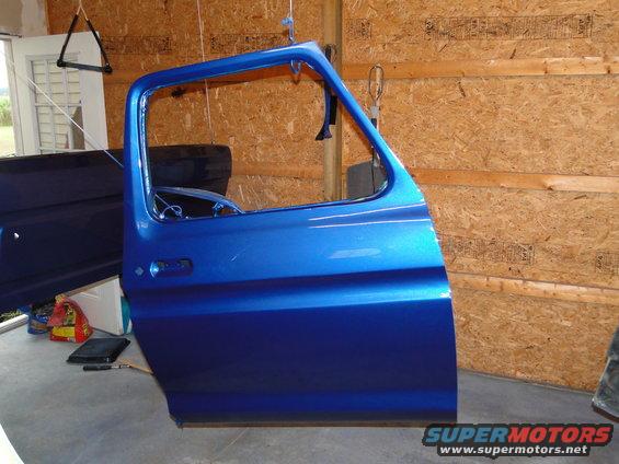 Blue car door hanging from a hook, showing fresh paint and interior details