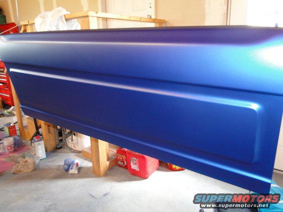 Blue tailgate with a recessed panel, resting on wooden sawhorses in a garage