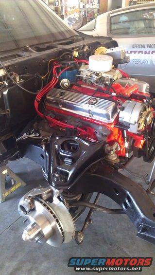 Engine and front suspension parts of a car, with brake rotor and caliper visible