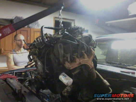 Man in garage with engine hoist lifting an engine out of a car