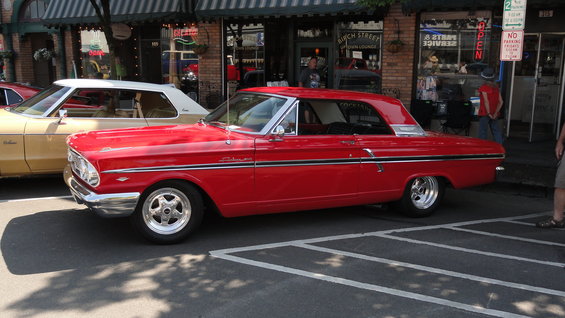 Red 1964 Ford Fairlane coupe parked next to a tan car on a street