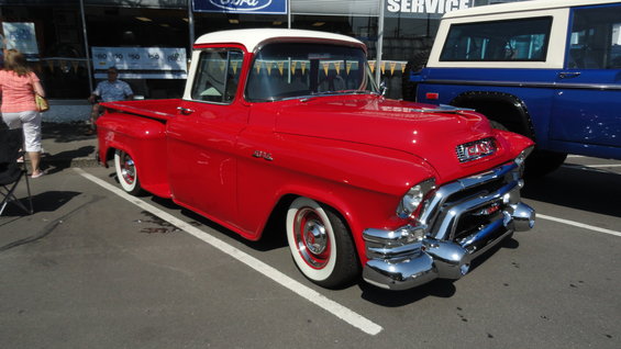 Red GMC pickup truck with white roof and wide whitewall tires. Blue SUV parked behind it