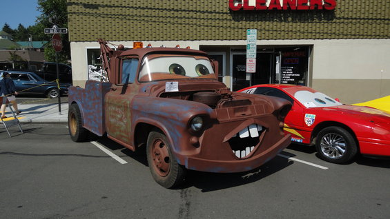 Rusty tow truck with cartoon face, hood open, parked next to a red sports car