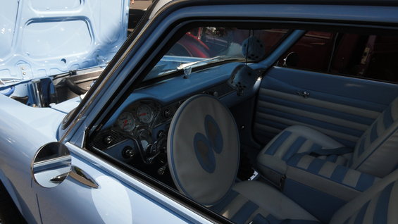 Interior of a light blue 1964 car with striped seats and a large steering wheel cover