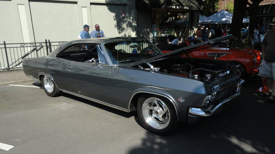 Dark gray 1965 Chevrolet Impala coupe with hood open, parked next to a red convertible