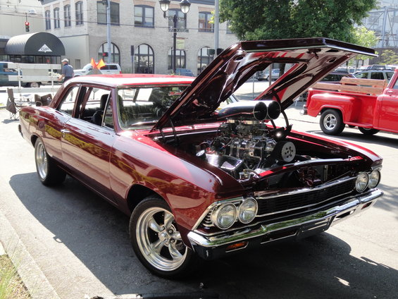Customized 1966 Chevrolet Chevelle SS with hood open, showing supercharged engine. Red pickup truck in background