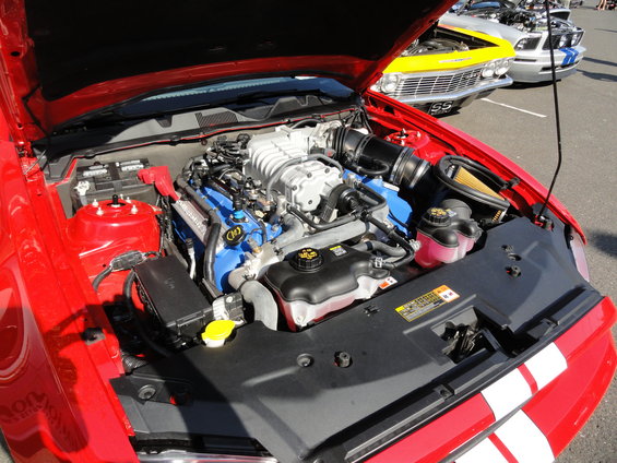 Red car's engine bay with a supercharger. Yellow and silver cars are in the background