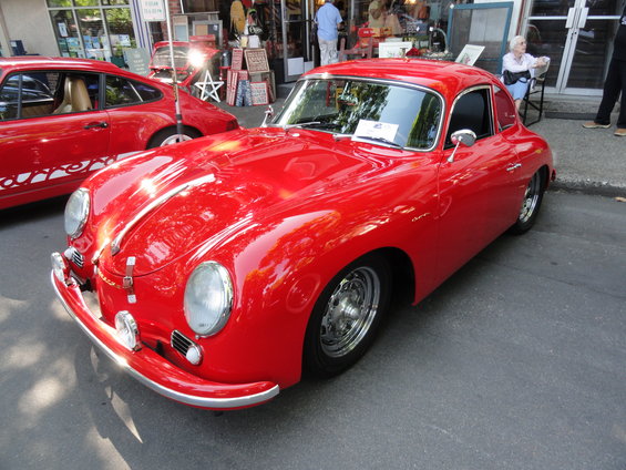 Red coupe with chrome bumper and headlights parked on asphalt. Another red car is visible to the left