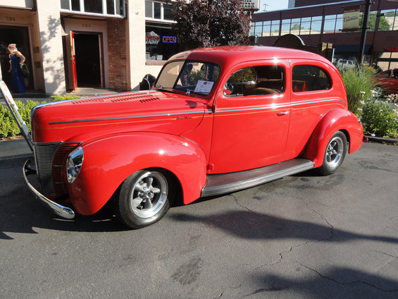Red sedan hot rod parked outside a building. It has a chrome bumper and silver wheels