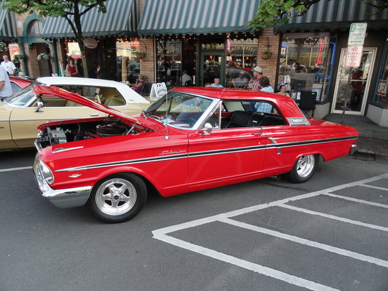 Red 1964 Ford Fairlane coupe parked on street, hood open, chrome wheels, black interior