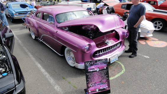 Purple 1954 Chevrolet Bel Air with hood open, parked at a car show. Sign in front says '1954 Chevrolet'