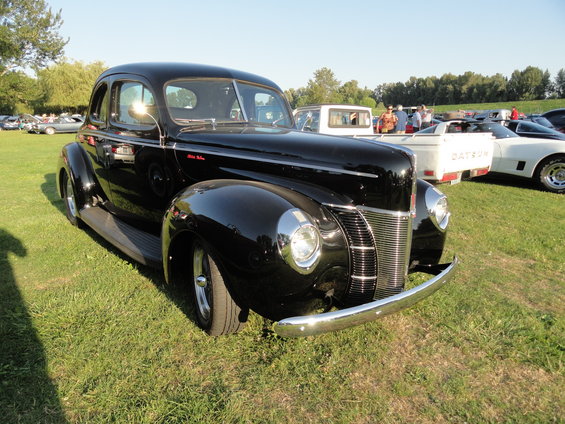 Black 1939 Ford Coupe parked on grass with other cars in background