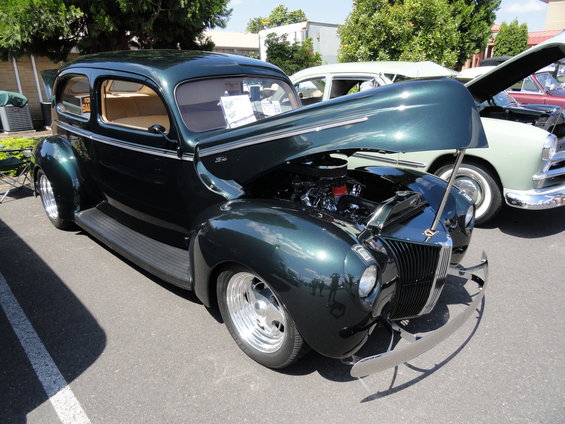 dark green sedan with hood open, showing engine. Another car is parked next to it